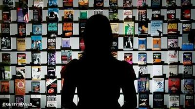 A person is silhouetted against an exhibition of James Bond book covers.