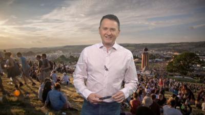 Matt Taylor standing in front of a picture of a field at Glastonbury