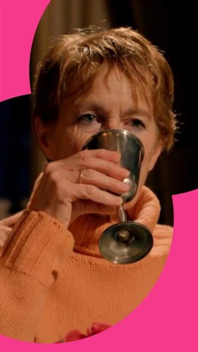 Celia Imrie holds a metal wine glass up to her face 