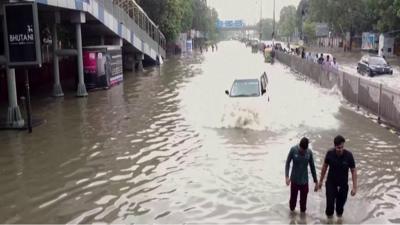 A car and people wading through the flood water