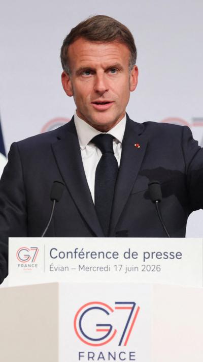 French President Emmanuel Macron holds a press conference during the G7 Summit, he speaks at a lectern and points with one hand.