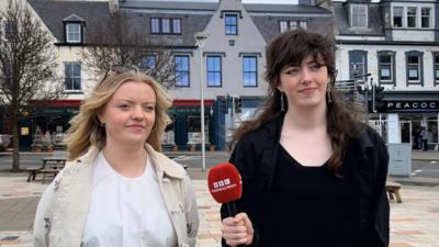 Sadie Drye agus Flòraidh Stevenson, a tha mar phàirt de Chomuinn Nàiseanta nan Oileanach, nan seasamh ann am baile Steòrnabhaigh.