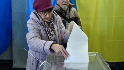 A voter attempts to post her comically long ballot paper in the ballot box