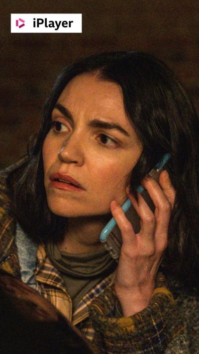 A woman with dark hair holds a phone to her ear and looks to the side.