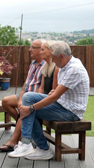 Two men and a woman sat on a garden bench.