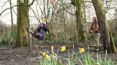 A little girl is swinging in a forest on a swing in front of a patch of daffodils