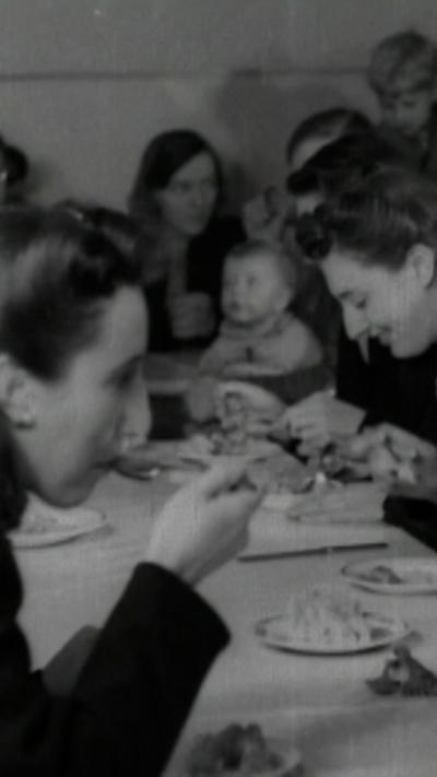 Women in the 1940s sit at a a long table, eating a meal