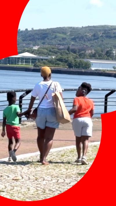 A mother walks her two children by the riverside.