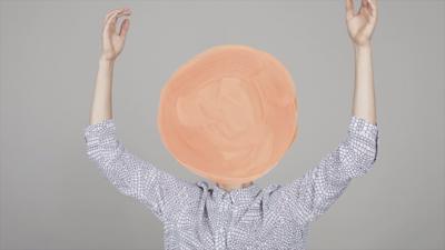Person with their arms in the air and their face painted over with a pink circle