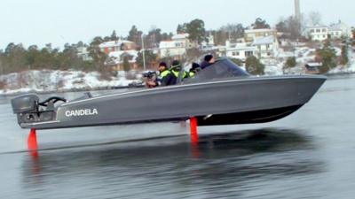 A grey electric boat with red hydrofoils lifts out of the water