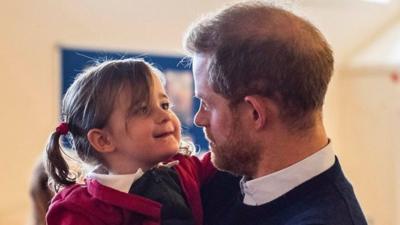 Prince Harry picks up a little girl at Windsor's Broom Farm Community Centre