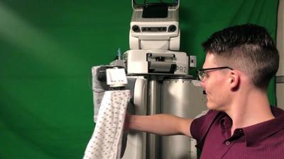 PR2 (a robot) helping a man put on a hospital gown