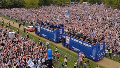 Blue smoke and cheers fill the air as people line the streets to greet their newly promoted heroes.