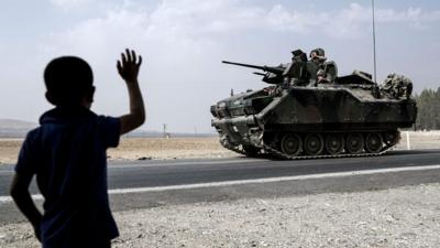 A child waves toward Turkish troops heading to the Syrian border