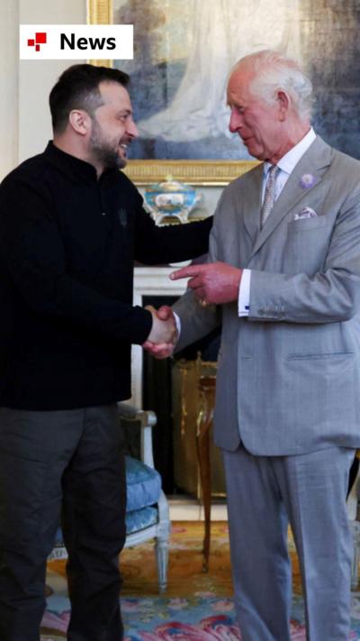 President Zelensky on the left wears a black jumper and shakes hands with King Charles who wears a grey suit.