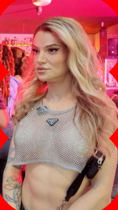A woman with long, blonde hair wearing a mesh crop top looks at someone off-camera.