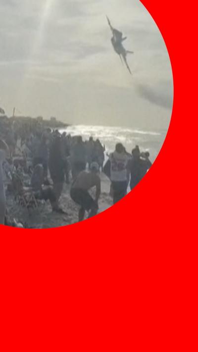 Jet flying above a crowd on a beach with a red circle around it.