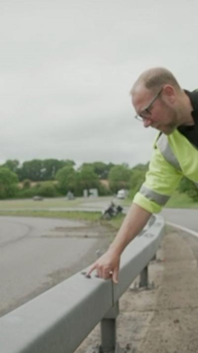 A man in hi vis pointing to a scuff on a road crash barrier