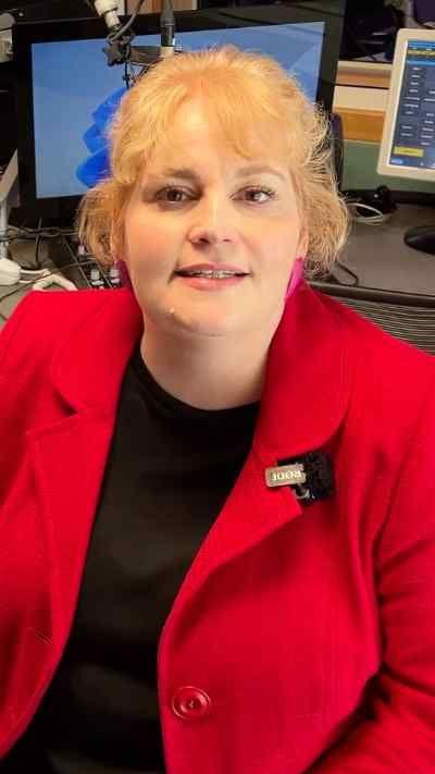 A woman in a red jacket with blonde hair sitting in front of a computer screen