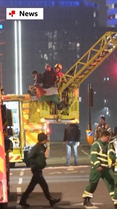 Emergency services in a cherry picker, near the road, with a man holding a Palestinian flag