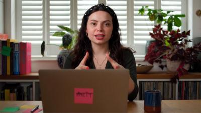Author Sophia Smith Galer sitting at a desk with her laptop open, looking into the camera.