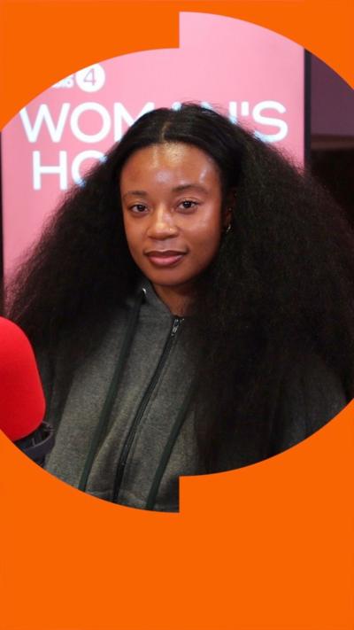 Tolu Coker wears a grey hoodie and sits behind a microphone. She has long black hair.