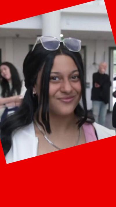 Student looks at camera - she has long dark hair and glasses on her head