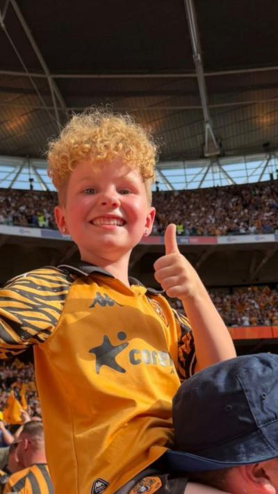 A young Hull City fan in the stadium giving a thumbs up.