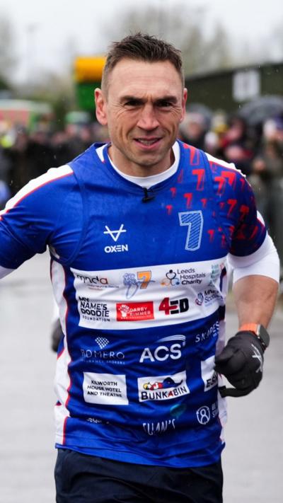 Kevin Sinfield running in a blue shirt with MND charities' logos on it 