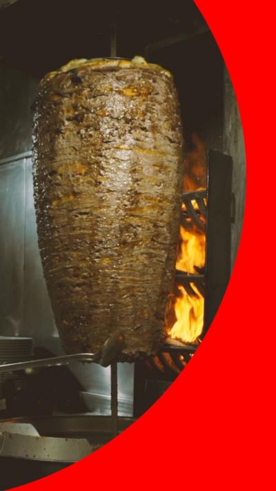 A hunk of doner meat slow cooks on a spit in front of an open flame.