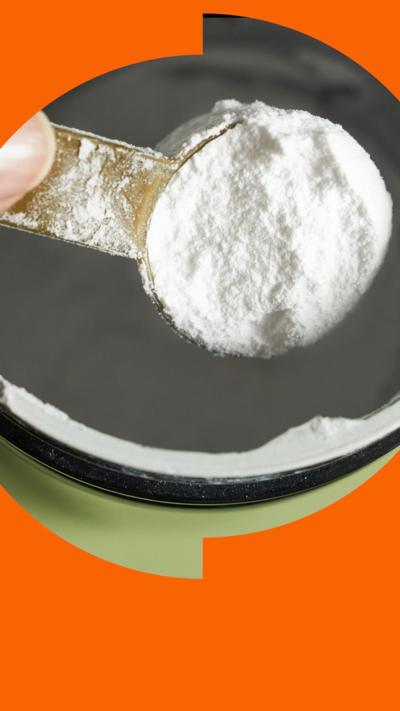 A close-up of a hand holding a spoonful of creatine powder in a metal jar