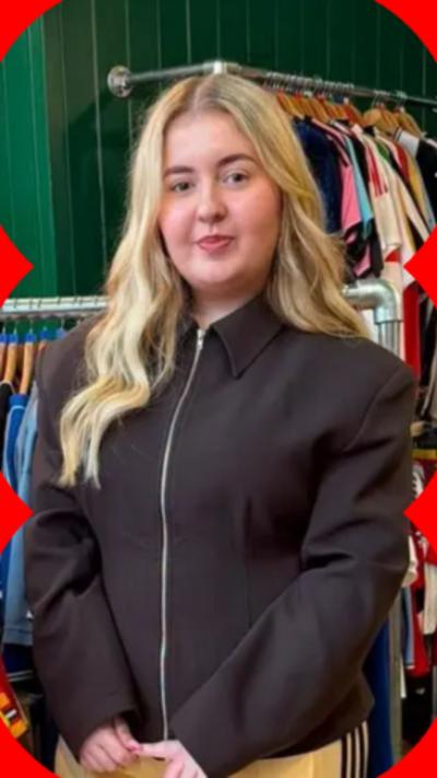A woman with long blonde hair stands in front of racks of football shirts 