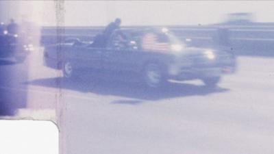 JFK's presidential limousine speeding along with a Secret Service agent clinging on