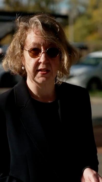 A woman with brown hair in a bob, wearing glasses and a black suit.