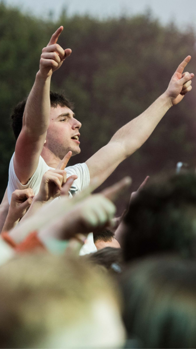 A young man sits on someone's shoulders with his hands in the air.
