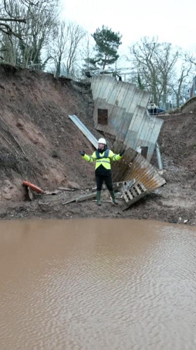 A man in a yellow hi vis jacket stood beside water in a hole after a canal subsided