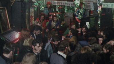 A crowd of people dance at a rock and roll pub. A band plays in the background