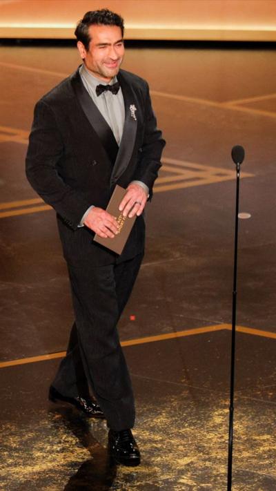Kumail Nanjiani is seen on stage in black tie holding an envelope at the Oscars.