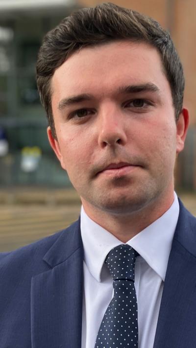 man with dark hair wearing a blue suit, shirt and tie