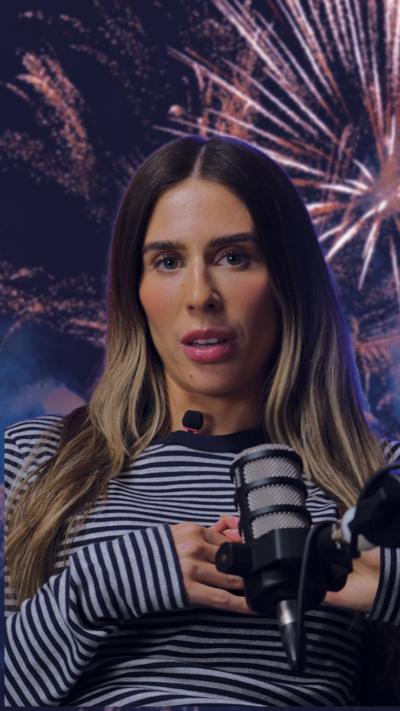BBC presenter looks at camera. She is wearing a black and white stripe top and is speaking into a microphone. There is an image of fireworks in the background.