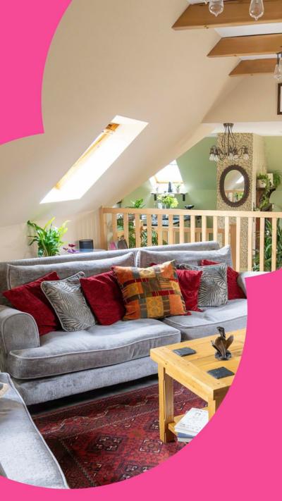 A room with three grey sofas angled at 45 degrees from the walls; there is a coffee table and red rug in the centre