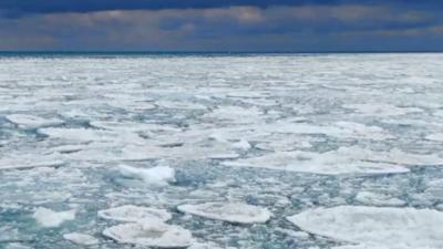 Ice sheets cover lake michigan on a cold, day with a blue sky and a string of clouds in the distance.