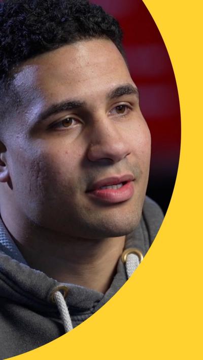 Delicious Orie looks off camera. He has short black hair and is wearing a grey hoodie with white drawstrings.