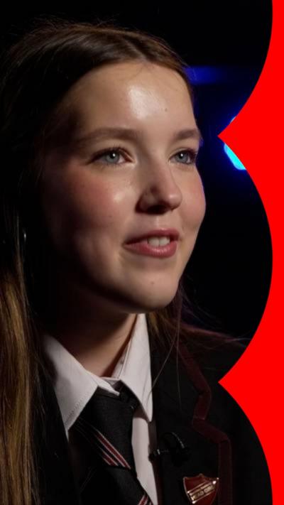 Student Tess smiles. She has long brown hair and wears a school uniform 