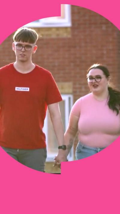 Ryan, wearing a red t-shirt, and Olivia, wearing a pink t-shirt, hold hands outside their house.