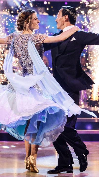 A woman in a pink ballroom dress dances with a man in a black tuxedo