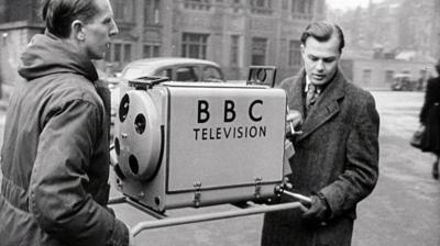 Two men carrying a large camera labelled '鶹Լ Television'.