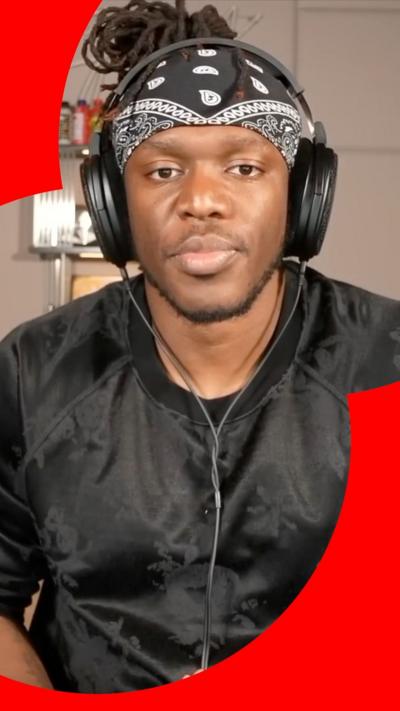 KSI looks at the camera. He wears a black jumper, black headphones and a black bandanna. 