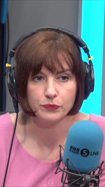 Bridget Phillipson in a pink top, wearing headphones in front of a blue microphone