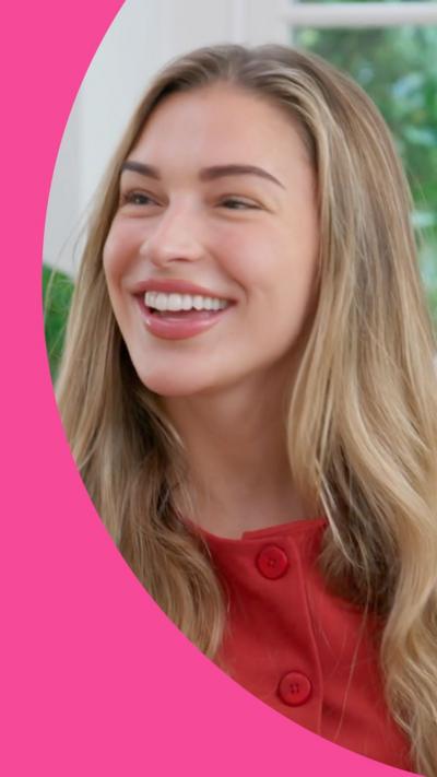 Zara McDermott has long blonde hair. She is wearing an orange-red button up top.